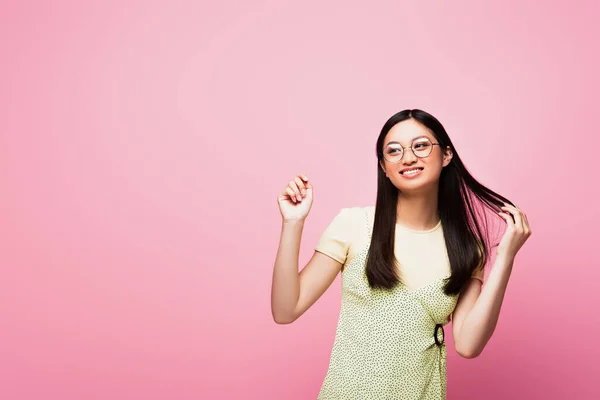 快乐而年轻的亚洲女人 戴着眼镜 触摸着头发 孤零零地看着粉红的脸庞 — 图库照片