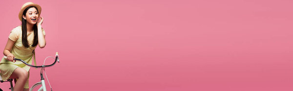 panoramic crop of excited asian young woman in straw hat near bicycle isolated on pink  