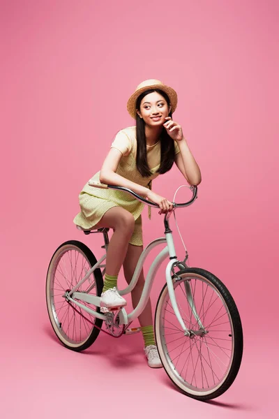 Χαρούμενη Ασιάτισσα Ψάθινο Καπέλο Κάνει Ποδήλατο Και Κοιτάει Αλλού Ροζ — Φωτογραφία Αρχείου