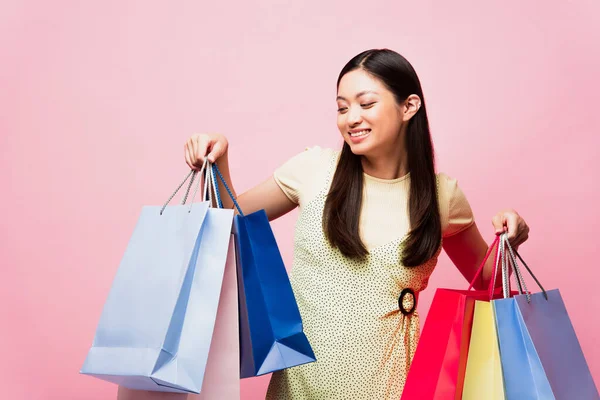 Glimlachende Jonge Aziatische Vrouw Zoek Naar Winkeltassen Geïsoleerd Roze — Stockfoto