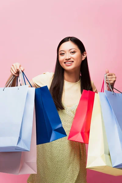 Glad Asiatisk Flicka Tittar Kameran Och Hålla Shoppingpåsar Isolerade Rosa — Stockfoto