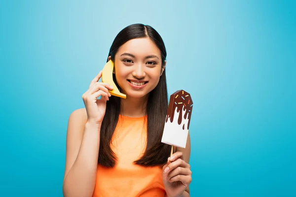 Счастливая Азиатская Девушка Держит Банан Возле Уха Бумажный Лед Крик — стоковое фото