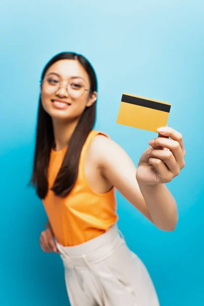 青の上にクレジットカードを保持しているメガネで幸せなアジアの女の子の選択的な焦点 — ストック写真