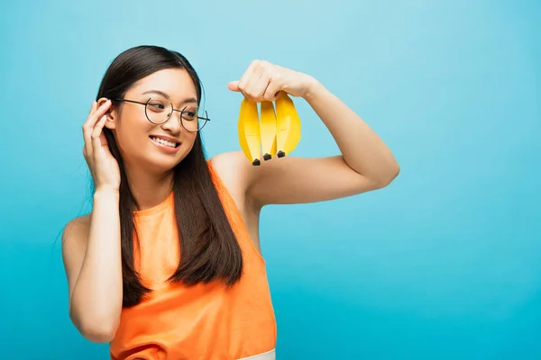 Щаслива Азіатська Дівчина Окулярах Дивиться Стиглі Банани Ізольовані Синьому — стокове фото