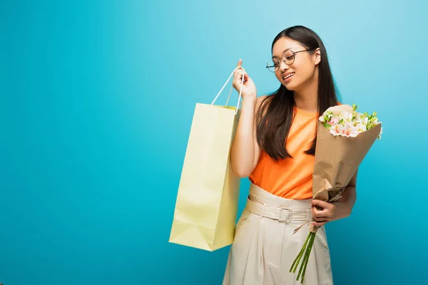 Cheerful Asian Woman Glasses Holding Shopping Bag Flowers Blue — Stock Photo, Image