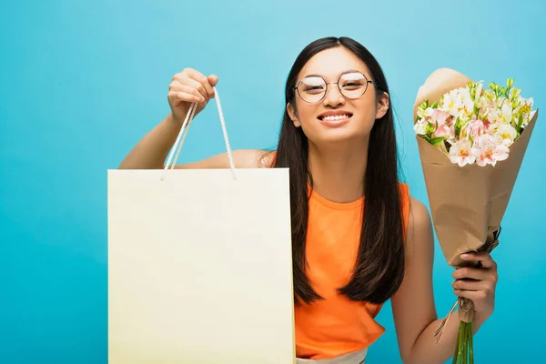 Позитивна Азіатська Жінка Окулярах Тримає Сумку Покупок Квіти Синьому — стокове фото