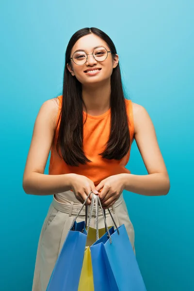 Positive Asian Woman Glasses Holding Shopping Bags Blue — Stock Photo, Image