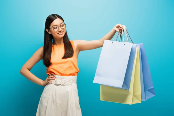 戴眼镜 提着购物袋 手托着屁股站在蓝色衣服上的亚洲女人 — 图库照片