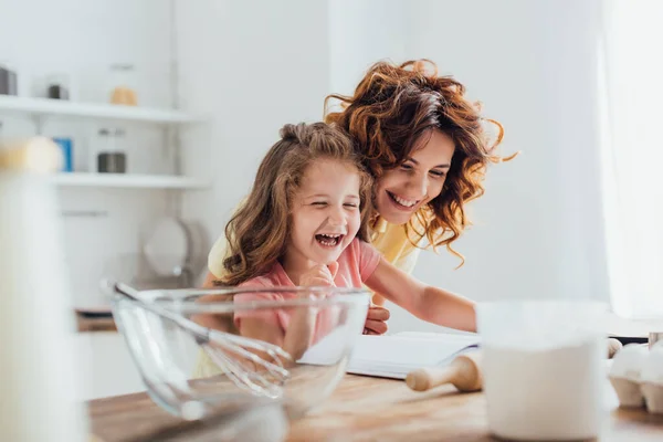 在阅读配料和炊具附近的食谱时 母亲和女儿笑的选择性焦点 — 图库照片