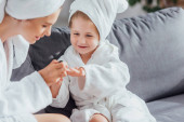selektivní zaměření mladé matky dělat manikúru na dceru v bílém županu a ručník na hlavě