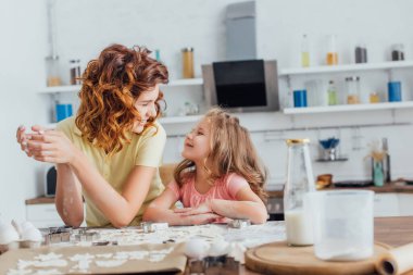 Genç anne ve kızı mutfakta kurabiye hazırlarken birbirlerine bakıyorlar.