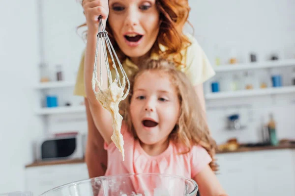 台所で調理中に泡立て器で生地を見て興奮した母親と娘の選択的な焦点 — ストック写真