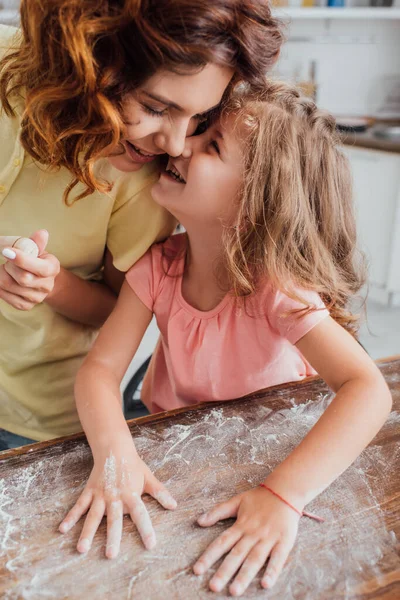 女儿一边和妈妈说话一边用面粉铺餐桌的高角镜 — 图库照片