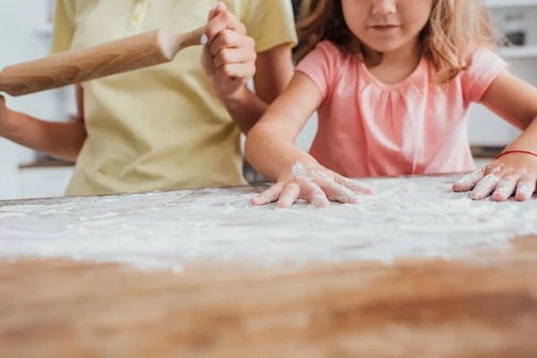 母親の近くの台所のテーブルの上に小麦粉を散乱少女のクロップドビュー圧延ピン 選択的フォーカス — ストック写真