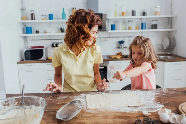 台所で母親に近い小麦粉でロール生地をカバーする女の子の選択的な焦点 — ストック写真