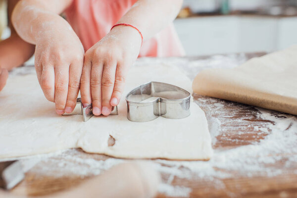cropped view of child cutting out cookings from rolled dough on table scattered with flour