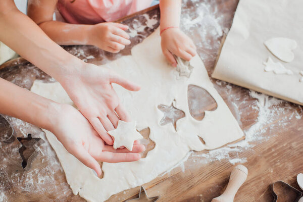 partial view of mother and daughter cutting out multi-shaped cookies from rolled dough