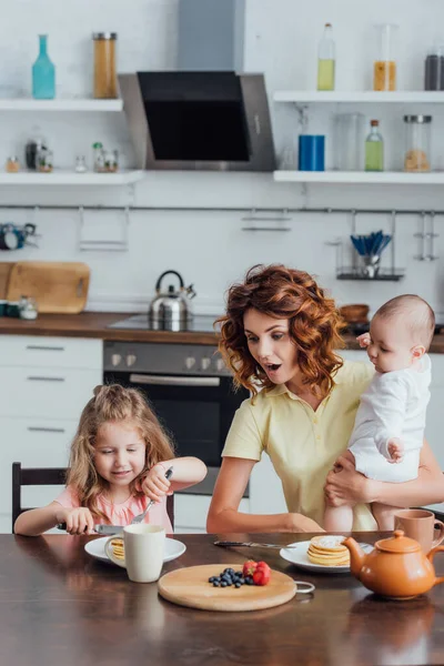 Surpresa Mãe Segurando Pequeno Filho Perto Filha Comer Panquecas Para — Fotografia de Stock