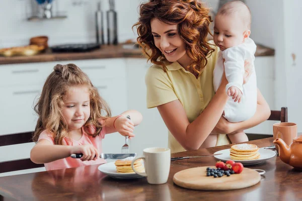 Ung Mor Håller Spädbarn Son Nära Dotter Äter Läckra Pannkakor — Stockfoto