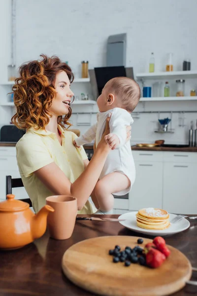 Junge Lockige Mutter Mit Säugling Tisch Serviert Mit Pfannkuchen Und — Stockfoto