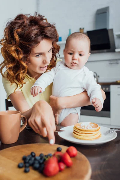 Selective Focus Young Mother Pointing Finger Fresh Berries Pancakes While — Stock Photo, Image