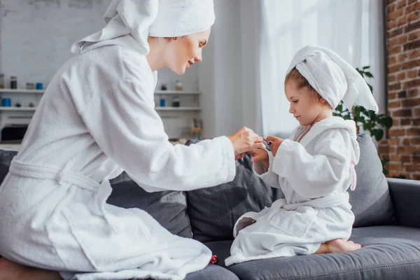 Daughter Making Manicure Mother While Sitting Together Sofa White Bathrobes — Stock Photo, Image