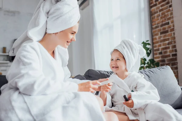 年轻女子穿着白色浴衣和毛巾坐在一起为孩子做指甲的选择性焦点 — 图库照片
