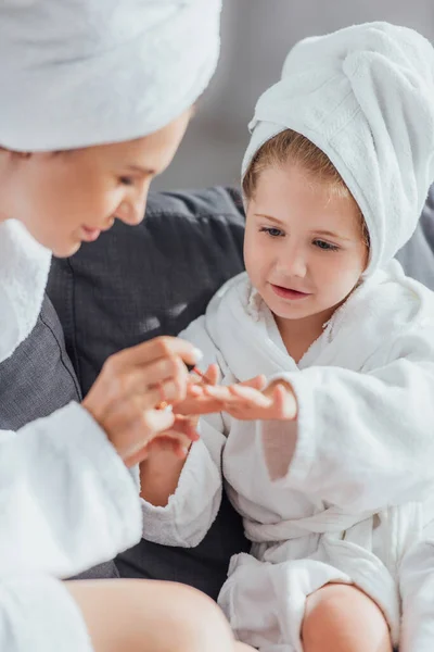 白いバスローブに座っている間に娘の爪にエナメルを適用する母親の選択的な焦点 — ストック写真