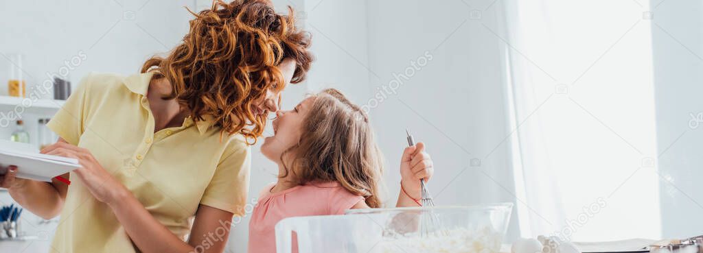 selective focus of mother standing face to face with daughter kneading dough in kitchen