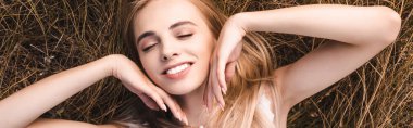panoramic concept of sensual blonde woman touching face while lying on grass with closed eyes, top view clipart