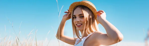 若いブロンドの女性の選択的な焦点は 麦藁帽子に触れ 青い空に対するカメラを見て パノラマの概念 — ストック写真