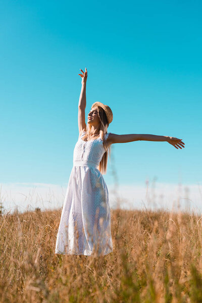 selective focus of sensual woman in white dress standing with outstretched hands and closed eyes on grassy field