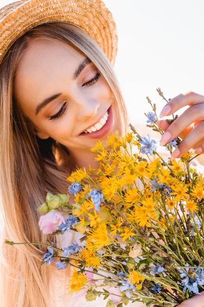 若いですブロンド女性でわら帽子タッチ花束の野生の花に対して明確な空 — ストック写真