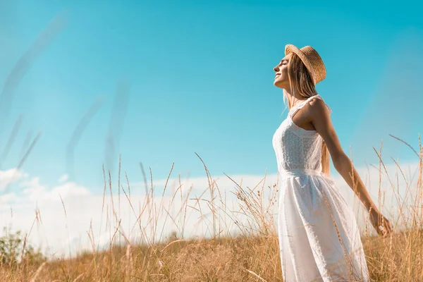 白いドレスを着たスタイリッシュな女性と草原で手と目を閉じて立つわらの帽子の選択的な焦点 — ストック写真
