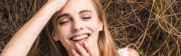 website header of excited young woman touching lips and forehead while lying on green grass, top view