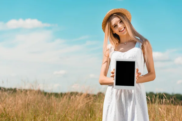 ストローハットとホワイトのドレスを着たブロンドの女性ファイルに立っている間に空白の画面でデジタルタブレットを示す — ストック写真