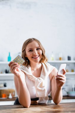 Elinde hap ve akıllı telefon dolu su toplayan genç bir kadın. 