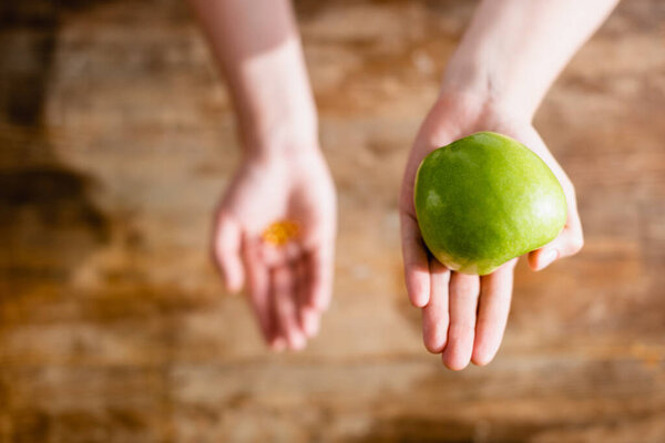 selective focus of woman holding apple and food additives in capsules 