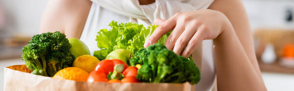 panoramic crop of young woman touching groceries in paper bag