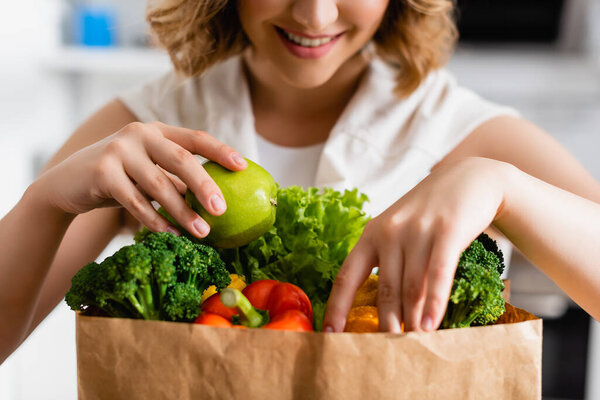 cropped view of woman touching apple and bell pepper in paper bag
