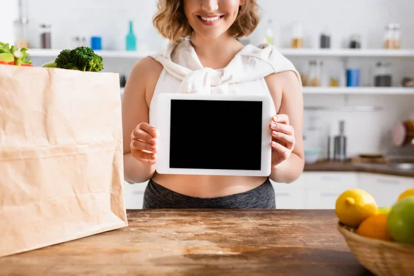 持空白屏幕数码平板电脑的妇女在装有杂货的纸袋附近的剪影 — 图库照片