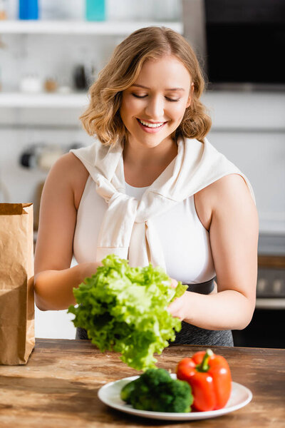 selective focus of woman holding fresh lettuce near vegetables on plate
