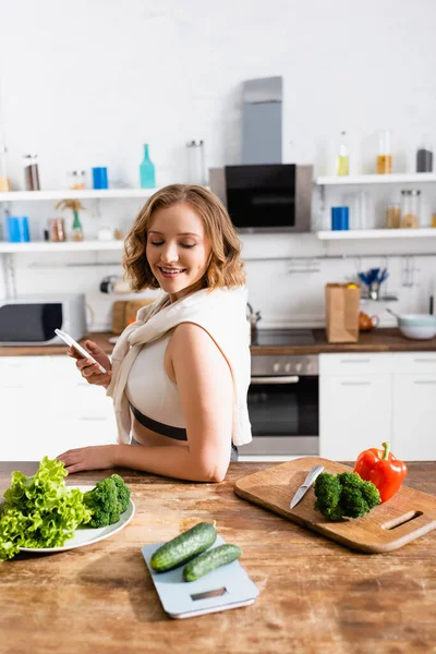 Mujer Sosteniendo Teléfono Inteligente Mirando Las Verduras Mesa — Foto de Stock