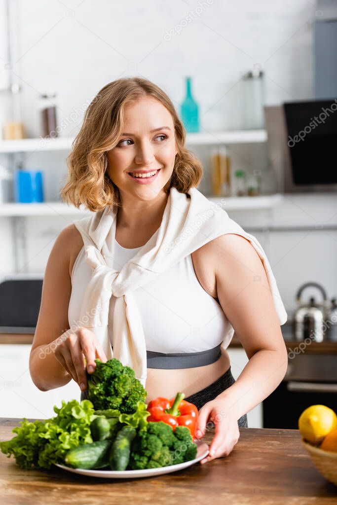 woman holding fresh broccoli near ripe vegetables on plate