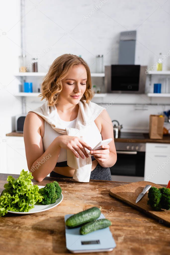 selective focus of woman using smartphone near green vegetables 