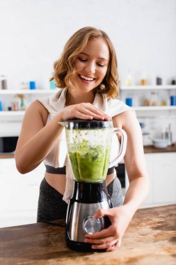 Blender 'da yeşil smoothie karıştıran genç kadın. 