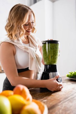 Blender 'da yeşil smoothie karıştıran kadın seçici odağı 