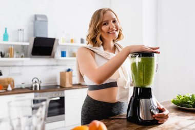 Blender 'da yeşil smoothie karıştıran genç bir kadının seçici odak noktası 