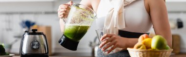 panoramic crop of young woman holding blender with mixed smoothie near glass  clipart