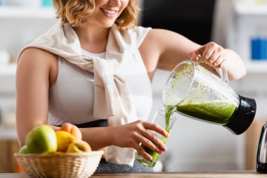 Bardağa karışık yeşil smoothie döken genç bir kadının kısmi görüntüsü 